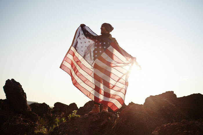 Person standing on rocks holding an American flag with sunlight, symbolizing surprisingly petty things people judge others for.