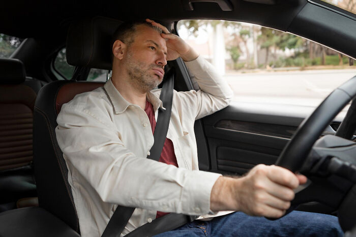 A stressed man driving a car with a frustrated expression, reflecting on petty things people secretly judge others for.