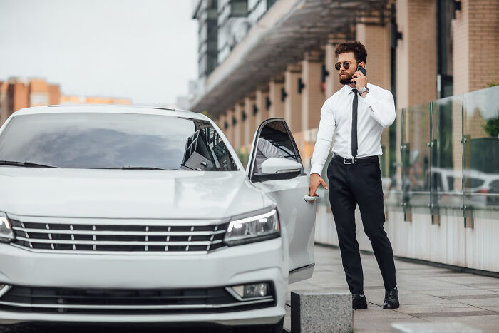 Man in formal wear opening car door and talking on phone, representing petty things people secretly judge others for.