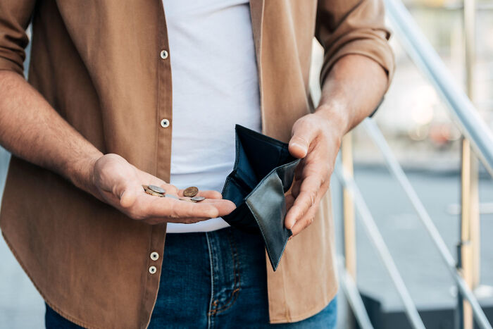 Person holding empty wallet with few coins in palm, illustrating surprisingly petty things people secretly judge others for.