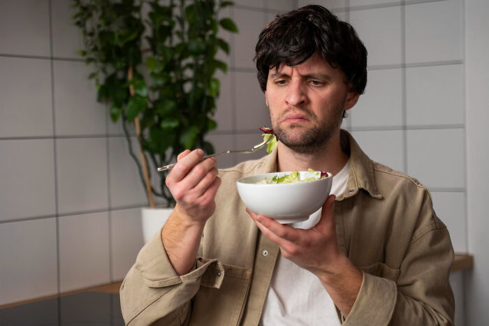 Man in casual clothes judging food on fork while holding a bowl, illustrating surprisingly petty things people judge others for