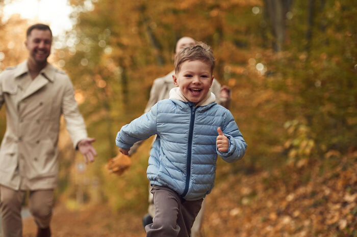 Young boy running joyfully in autumn forest with adults behind, illustrating surprisingly petty things people secretly judge.