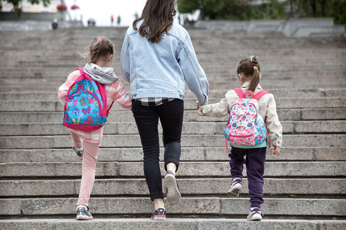 Woman and two kids carrying backpacks walking up stairs, illustrating surprisingly petty things people judge others for.