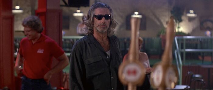 Man wearing sunglasses and dark jacket standing in a bar, capturing the theme of uncomfortable and messy secrets confessed anonymously.