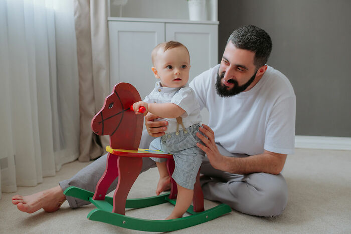 Man playing with toddler on a wooden rocking horse, capturing messy secrets childhood moments in a cozy room.