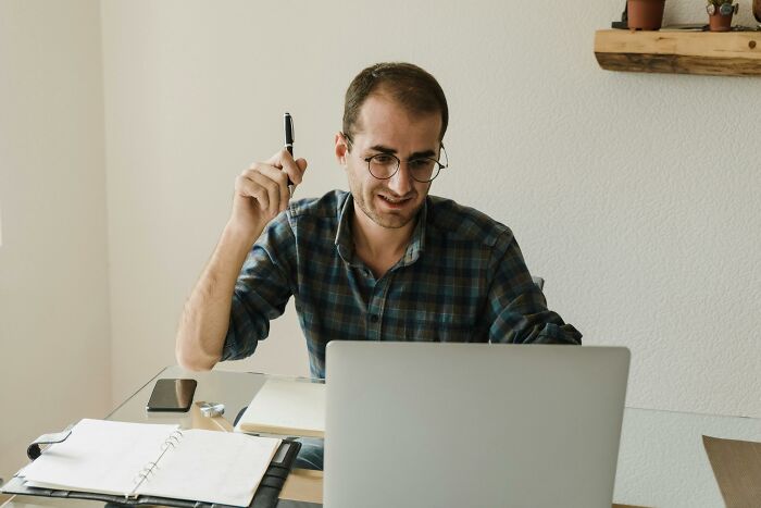 Man wearing glasses and plaid shirt holding a pen while working on laptop, reflecting on uncomfortable and messy secrets.