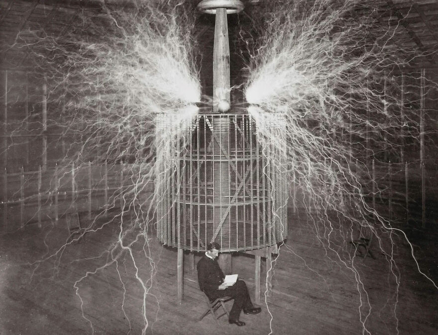 Man sitting near a large electrical coil emitting powerful sparks, illustrating strength and energy like a gigachad.