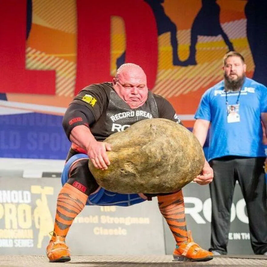 Strongman lifting a massive stone at a competition, showcasing power and strength admired by gigachads worldwide.