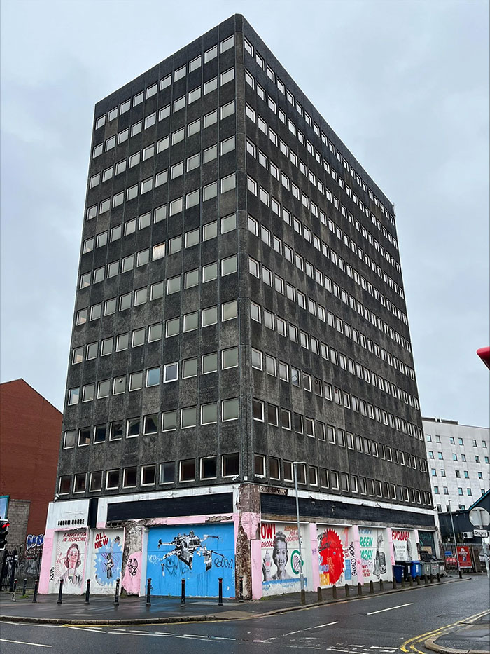 Large dark gray building with numerous windows and graffiti-covered lower walls, an example of architectural malpractice.