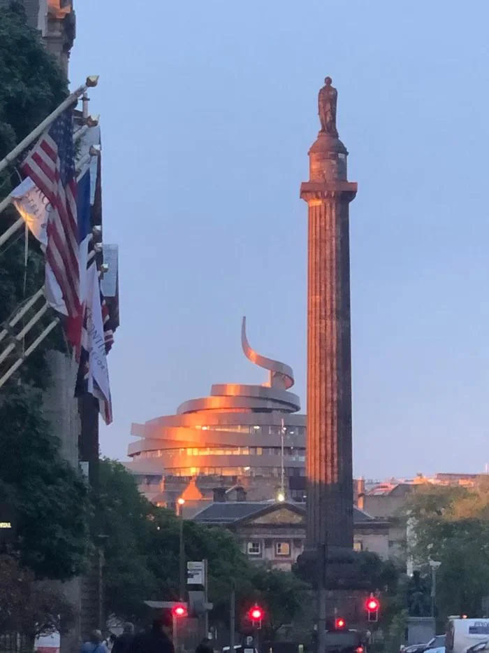 Modern architectural malpractice building with a spiral design reflecting sunset light behind a historic column monument.