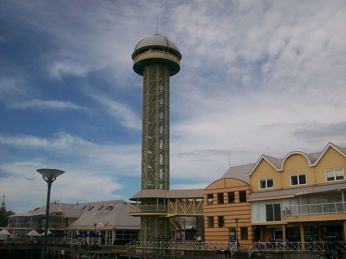 Tall observation tower with a dome top beside old-style buildings under a cloudy sky, illustrating architectural malpractice.