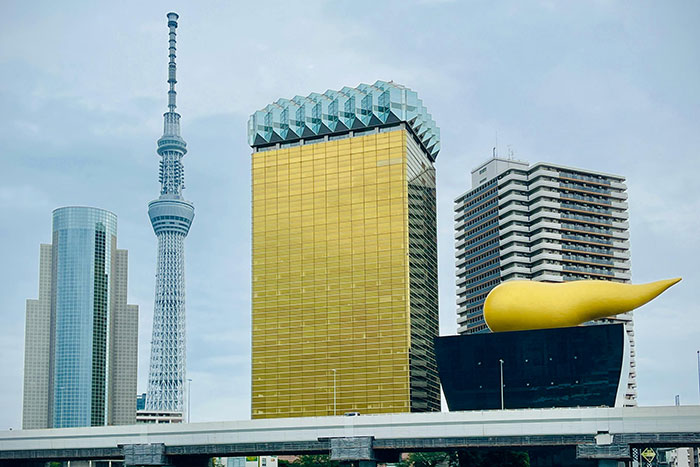 A cluster of buildings with unusual designs, including a golden tower and a structure with a large yellow ornament seen against a cloudy sky.