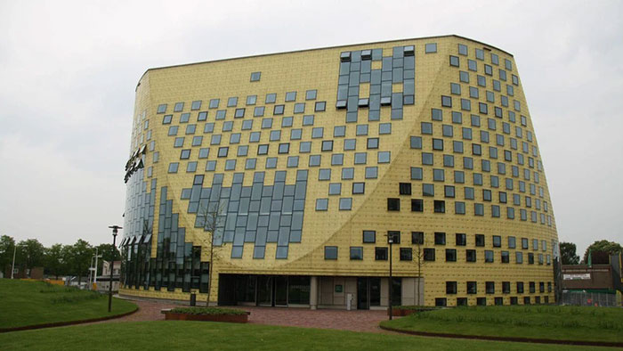 Modern architectural malpractice building with irregular glass windows and a yellow exterior, controversial design upsetting locals.