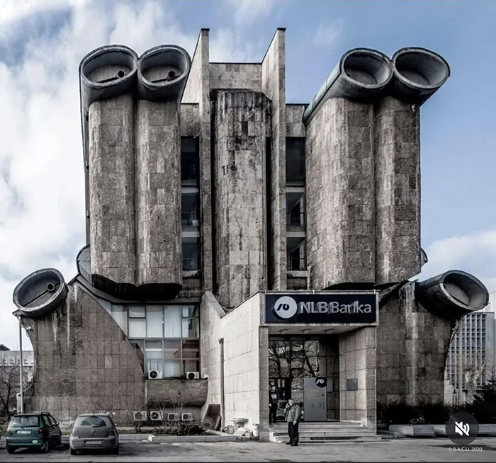 Brutalist architectural malpractice building with large cylindrical concrete vents, weathered facade, and bank entrance in an urban setting.