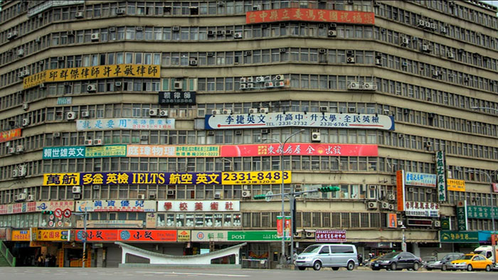 Large ugly building with numerous signs and worn exterior, an example of architectural malpractice costing billions.