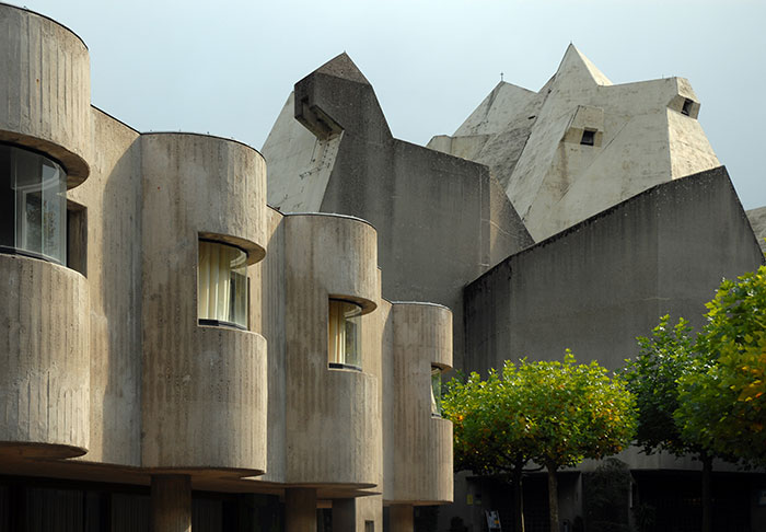 Brutalist architectural malpractice with unusual concrete structures surrounded by trees under a cloudy sky in urban area.