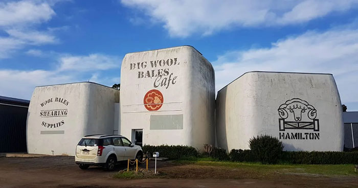 Three large, oddly shaped buildings resembling wool bales with signage, an example of architectural malpractice and ugly design.