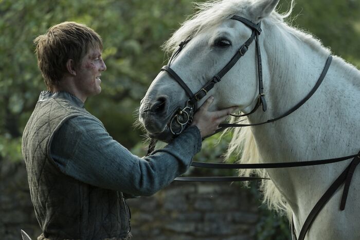 Actor interacting with a white horse on set for A Knight Of The Seven Kingdoms Season 2 filming outdoor scene.