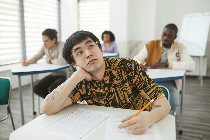 Student in classroom looking thoughtful while answering UK school science questions test on paper. Student in classroom looking thoughtful while answering UK school science questions test on paper.