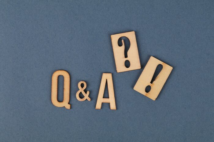 Wooden letters and symbols forming Q & A with question and exclamation marks on a gray background for general knowledge quiz.