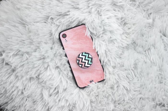 Smartphone with pink case and zigzag pop socket lying on fluffy white fabric, highlighting unhinged ways women traumatized men.