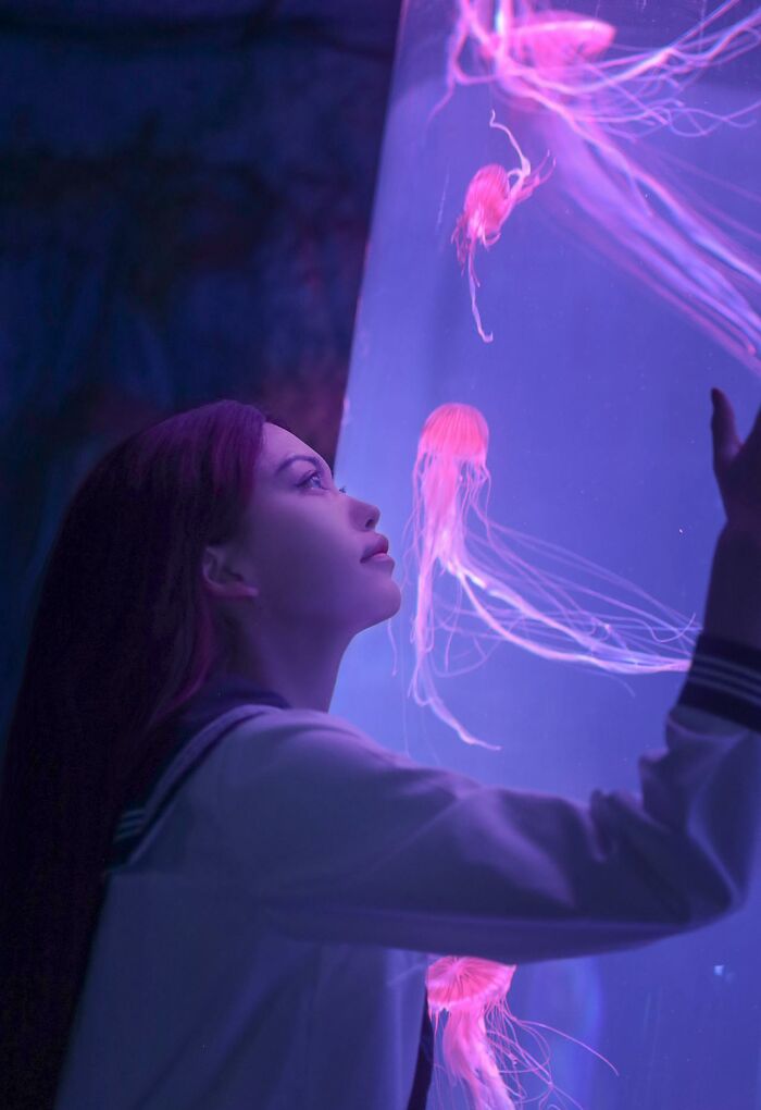 Young woman fascinated by glowing jellyfish in aquarium, capturing moments that make people pause and reflect on stupid things said.