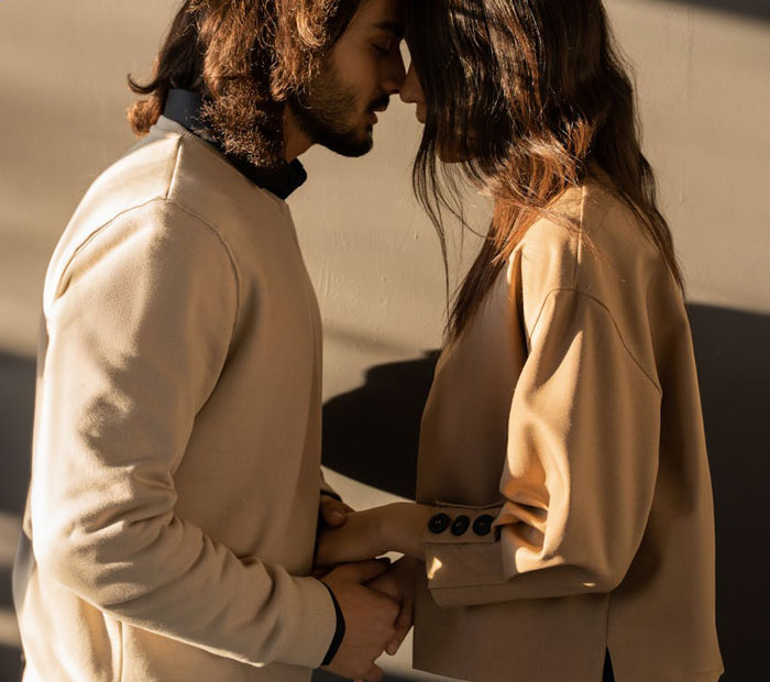 Young couple holding hands and touching foreheads, representing man wanting to move in with girlfriend but refusing her apartment.