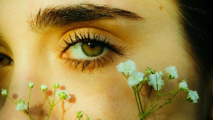 Close-up of a person's green eye with delicate white flowers nearby, challenging face reading skills better than an iPhone.