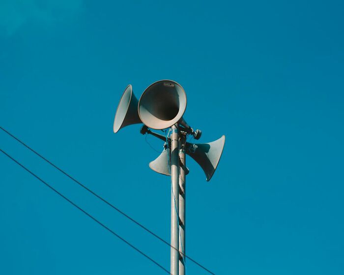 Outdoor emergency loudspeakers on pole against clear blue sky, symbolizing chilling sounds signaling immediate disaster.