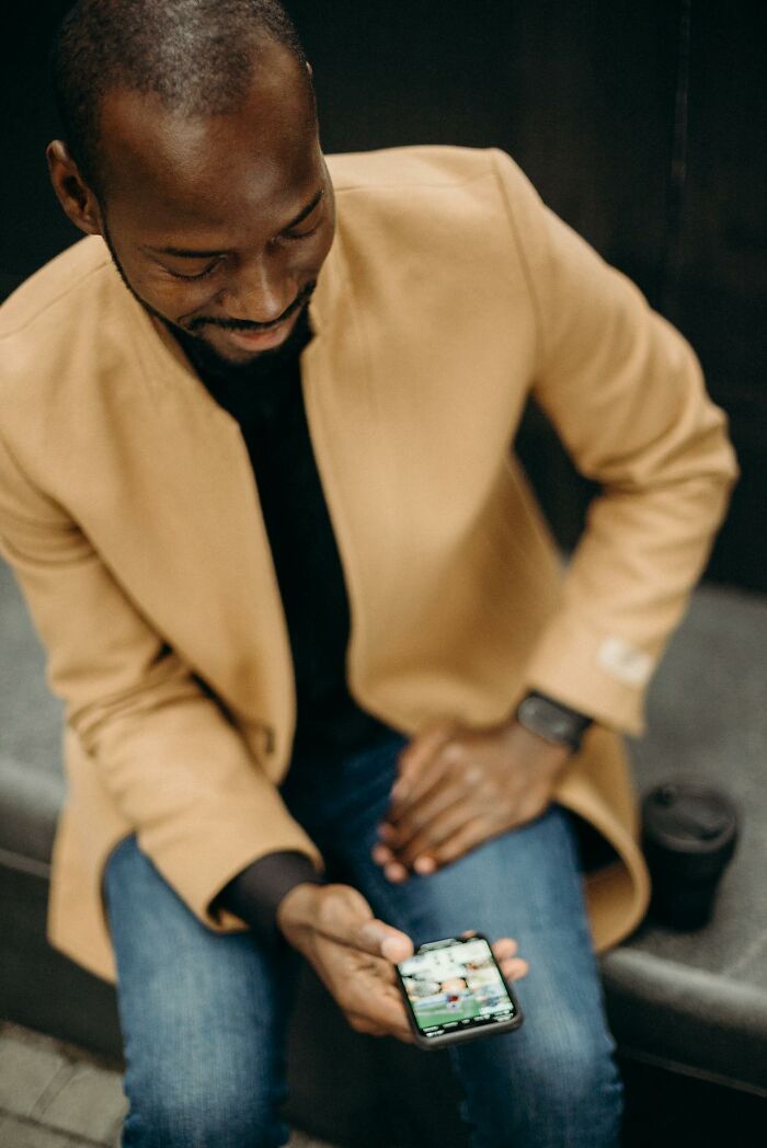 Man in tan coat and jeans looking at smartphone, illustrating people silently judge others in everyday situations.