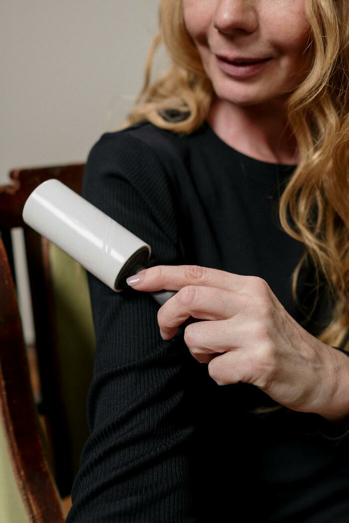 Woman using a lint roller on black sweater, illustrating a funny and harmless conspiracy theories concept.
