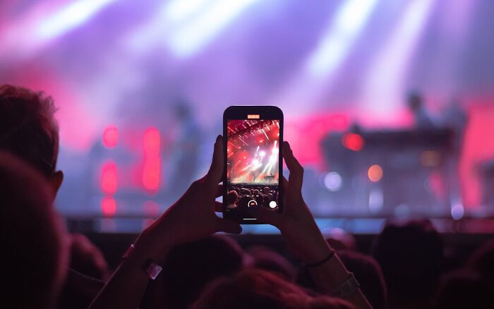 Person holding smartphone recording a live concert with colorful lights, reflecting silent judgment themes on behavior and people.