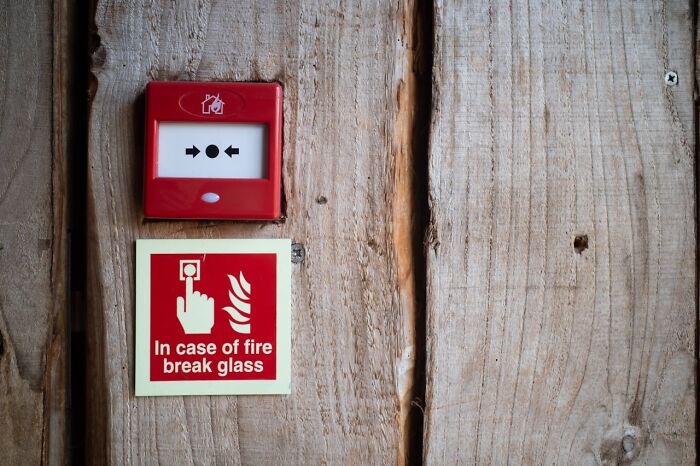 Red fire alarm and break glass sign mounted on a wooden wall signaling immediate disaster warnings.