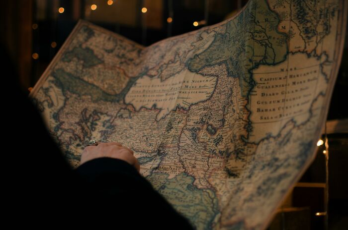Person holding and examining an antique world map featuring Afghanistan among 30 countries to identify on the map.
