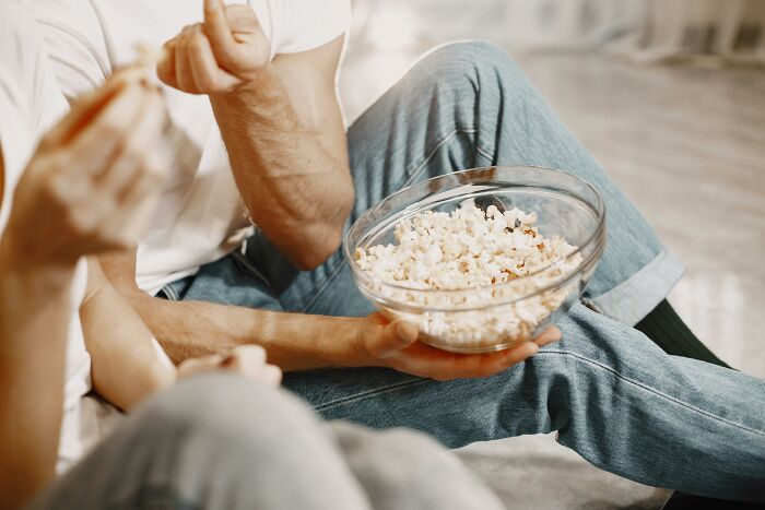 Two people sitting on the floor sharing a bowl of popcorn while watching movies, referencing popular films AITA descriptions. Two people sitting on the floor sharing a bowl of popcorn while watching movies, referencing popular films AITA descriptions.