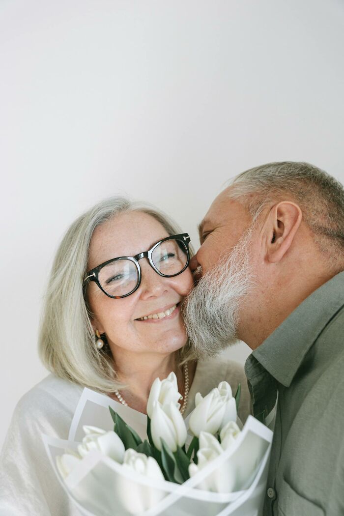 Older couple showing respect and love, with the man kissing the woman who holds a bouquet of white tulips.