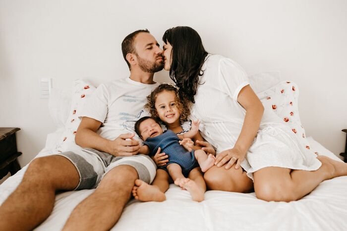 A married couple with their two children sitting on a bed, showing family love and respect in a cozy home setting.