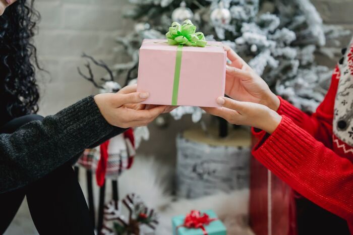 Two people exchanging a wrapped gift near a decorated Christmas tree, reflecting silent judgment moments.