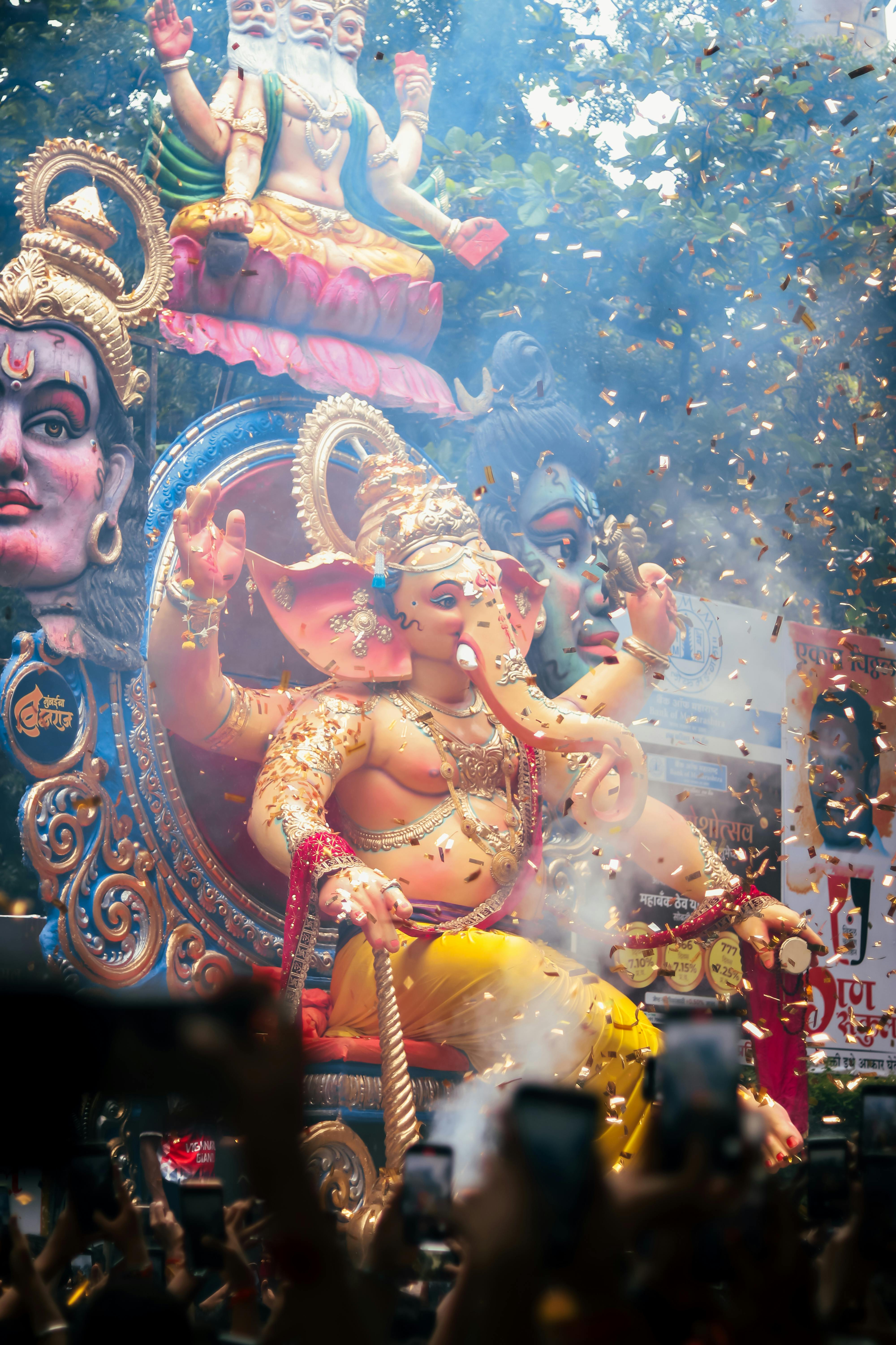 Large colorful statue of Lord Ganesha at a vibrant spiritual tourism festival in India with confetti and crowd photos.