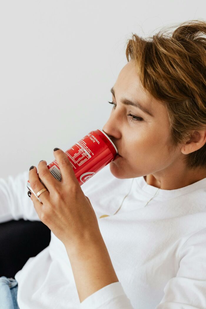 Person in white shirt drinking soda, appearing tired, representing graveyard shift workers during late hours.