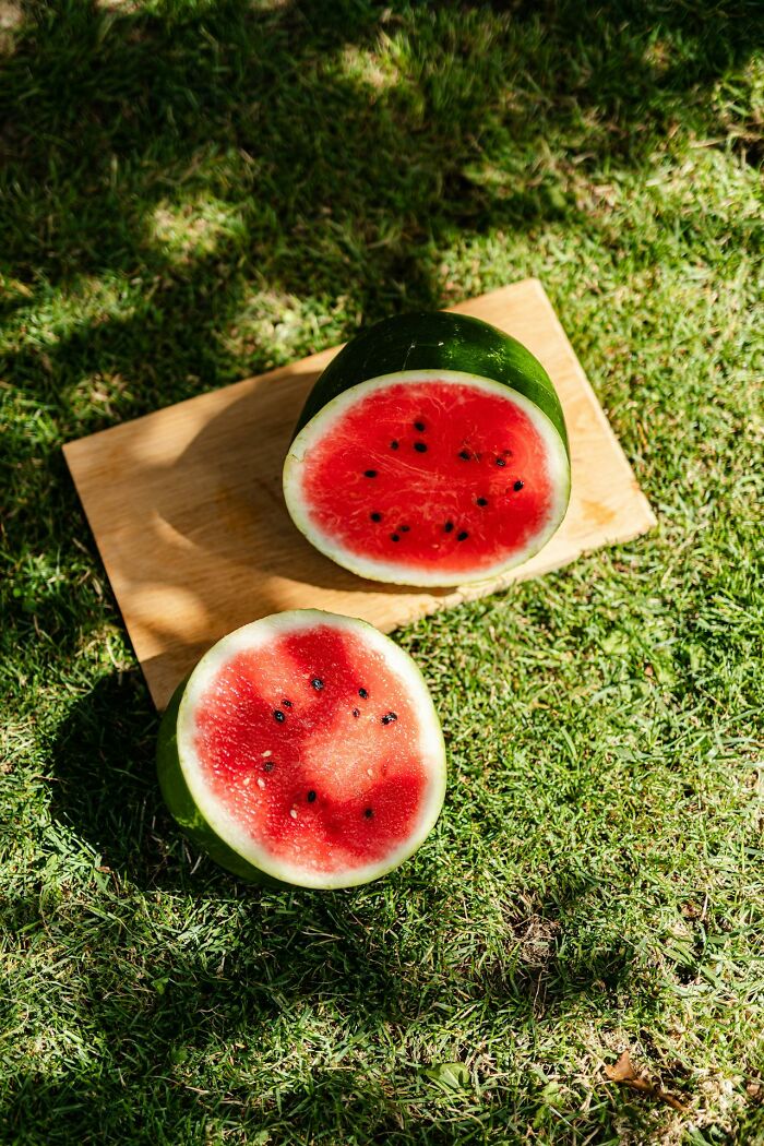 Watermelon cut in half on a wooden board outdoors on green grass, capturing a natural and fresh summer vibe.