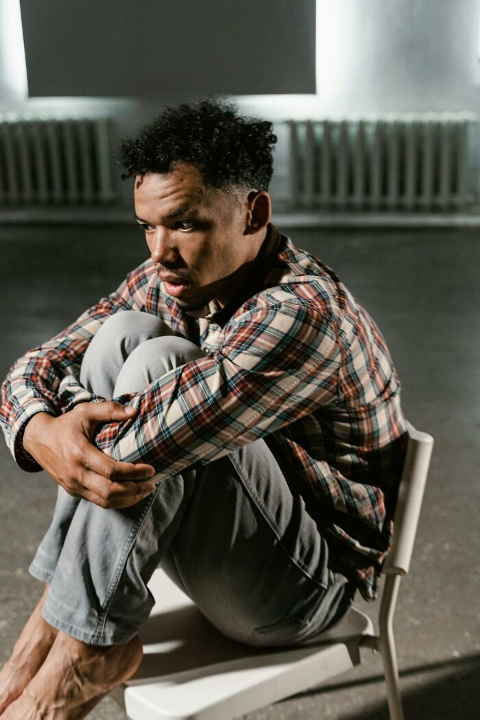 Man in plaid shirt looking scared and confused during a graveyard shift, sitting curled up on a chair in dim light