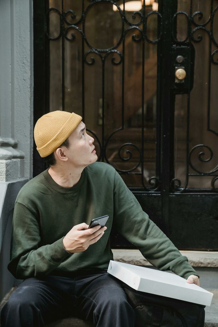 Young man in a yellow beanie holding a phone, looking up with concern, capturing the chilling sounds signaling disaster.