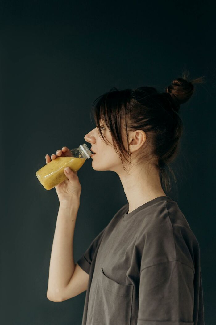 Young woman with hair in a bun drinking a yellow smoothie, illustrating today I learned facts for conversations.