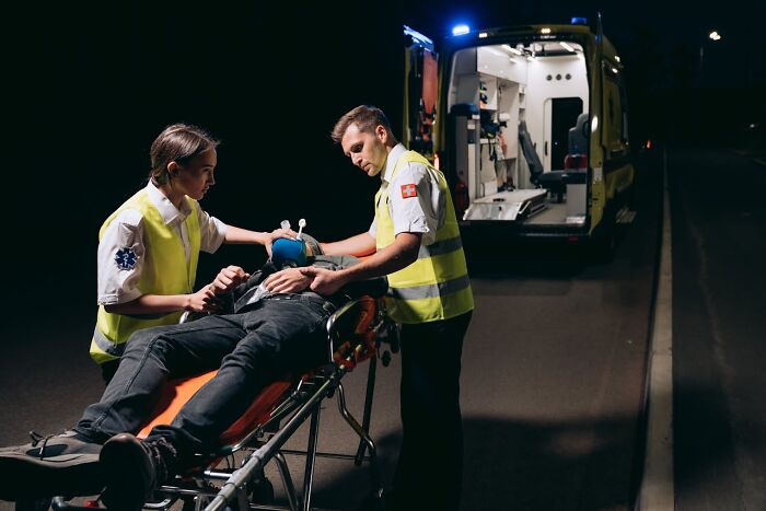 Two graveyard shift workers in reflective vests attending to a patient on a stretcher at night near an ambulance.