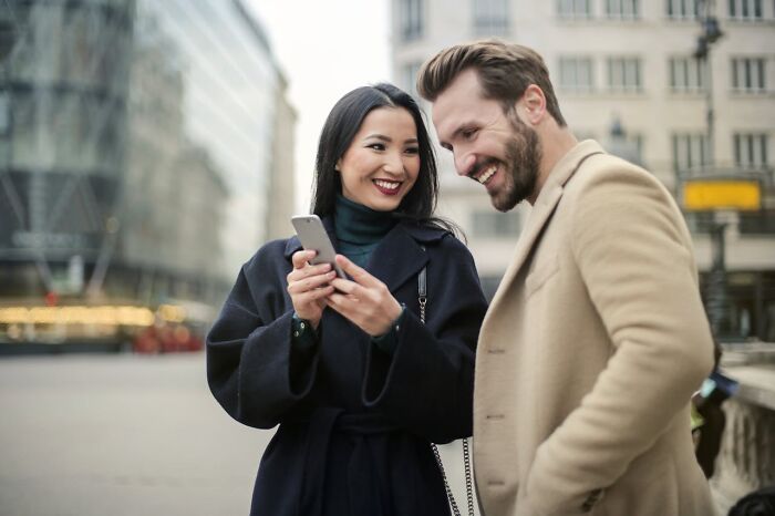 A smiling woman showing a phone to a married man in an urban setting, illustrating respect in relationships.
