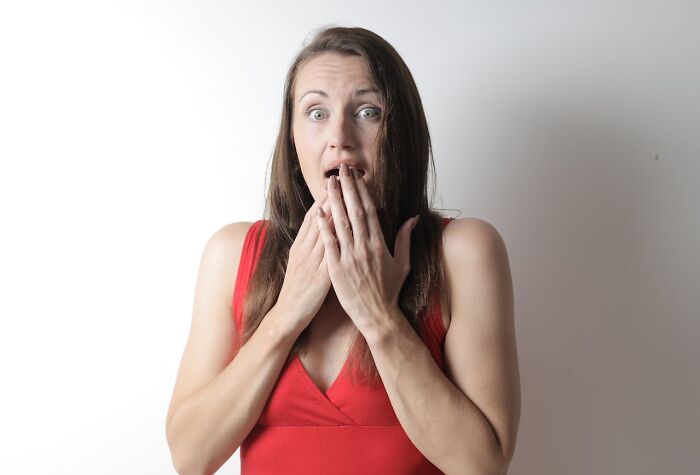 Woman in red dress looking shocked with hands covering mouth, expressing disbelief after hearing stupid things said by others.