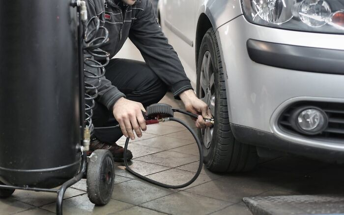 Mechanic using air compressor to inflate a car tire, highlighting chilling sounds that signal immediate disaster warning.