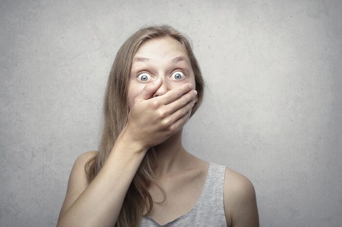 Woman with wide eyes covering her mouth, expressing shock from chilling sounds signaling immediate disaster.