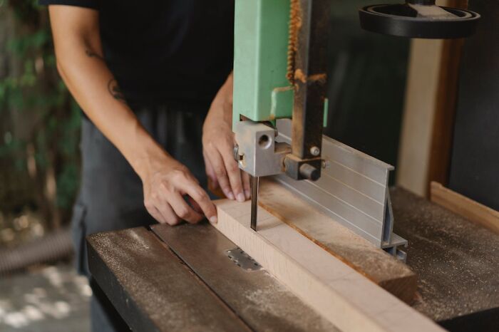 Person using a band saw to cut wood, illustrating the chilling sounds that signal immediate disaster in a workshop setting.